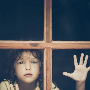 Young child looking through window with hand on glass, representing the journey of overcoming fear with divine help and daring to dream