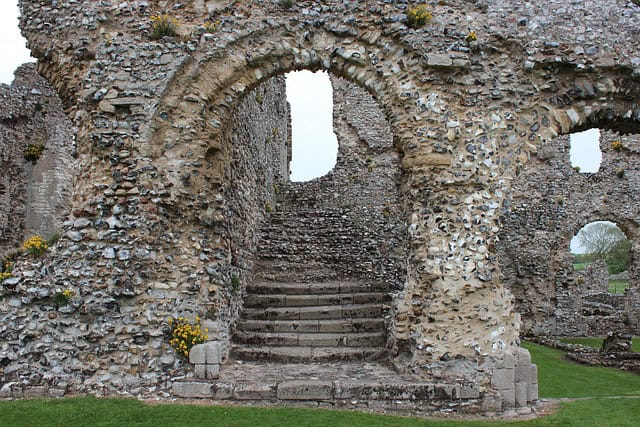 Weathered temple stairs ascending through stone archways toward light, the climb upward on the Sacred Way