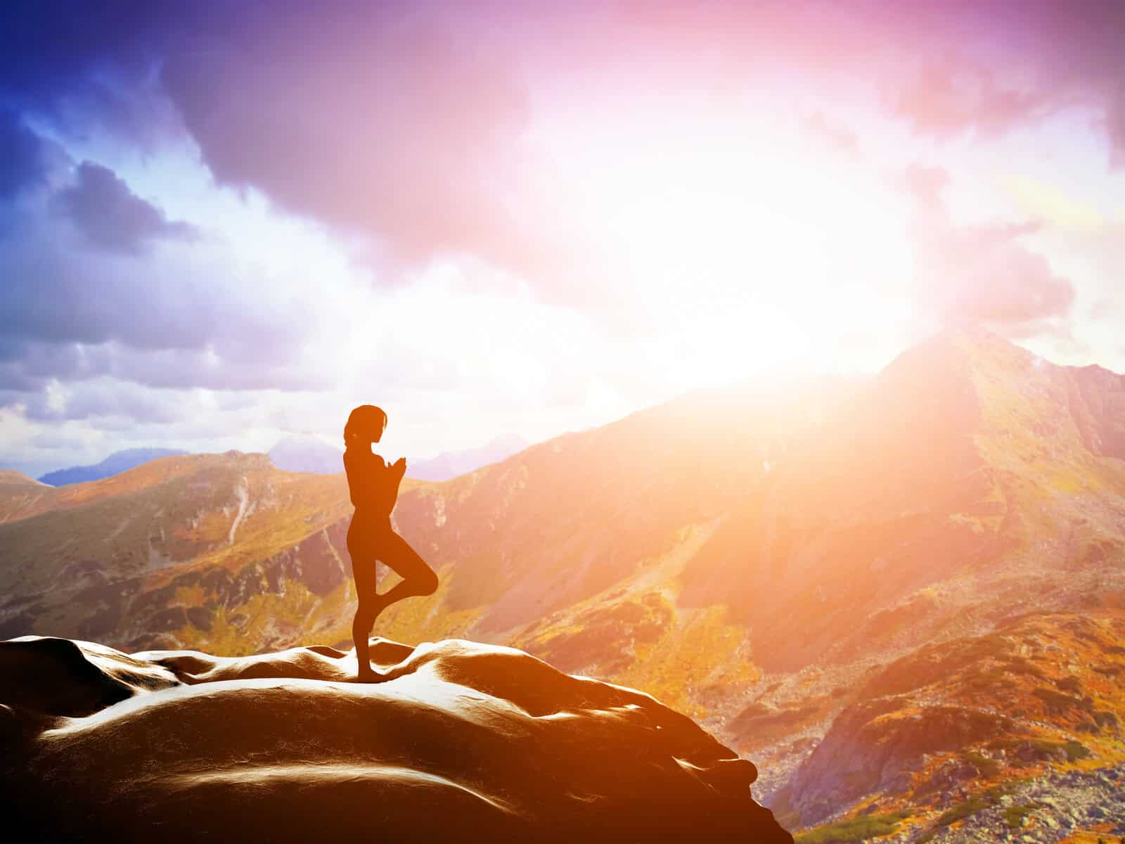 Silhouette figure in meditation pose on mountain peak at golden sunrise - representing spiritual emergence and awakening