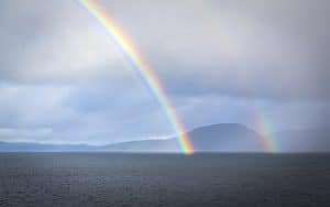 Double rainbow arcing over misty ocean waters and distant mountains - layers of sacred beauty in nature