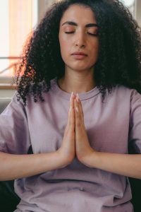"Person in lavender clothing sitting in meditation pose with hands in prayer position at heart center, eyes closed, creating internal altar space without external props"