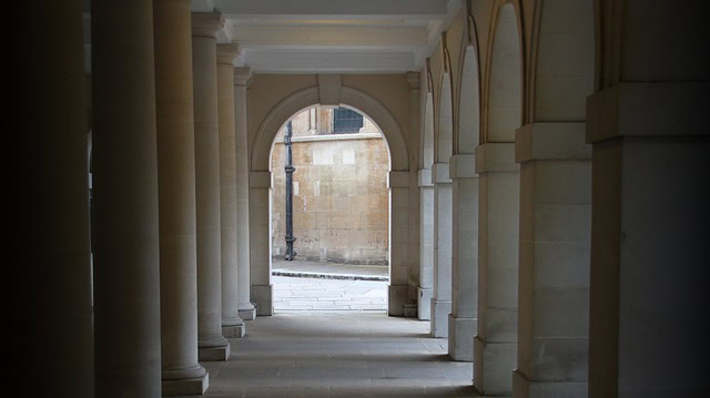 Ancient stone colonnade with sunlit arched passage inviting seekers to enter the Sacred Way of Apollo