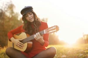 Teenage girl with long dark hair playing classical guitar at sunset, photographed from behind with the sun creating a golden halo behind her, representing divine-human collaboration in music
