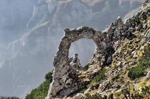 A natural stone arch window carved into a rocky mountain ridge with misty mountain peaks beyond