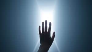 A silhouetted hand reaching toward radiant light, representing the choice to surrender and accept the sacred mantle of oracle for Apollo