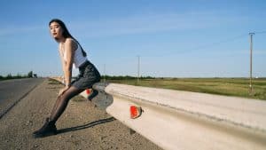 Woman sitting on a roadside guardrail, stuck on the side of the road, life passing by